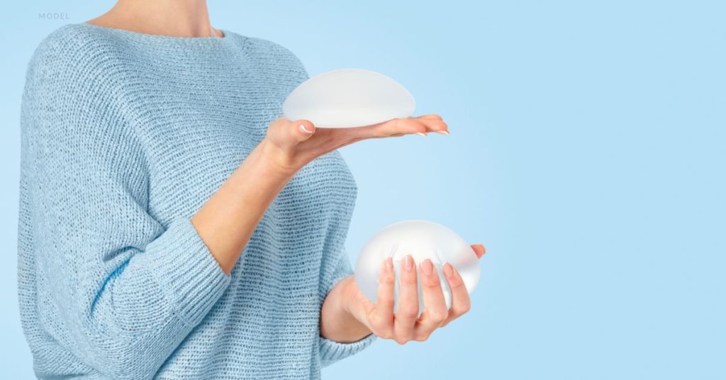 woman (model) holding breast implants as she tries to decide which option to choose