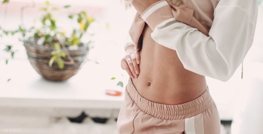 Woman lifting shirt to show tummy tuck results (model)