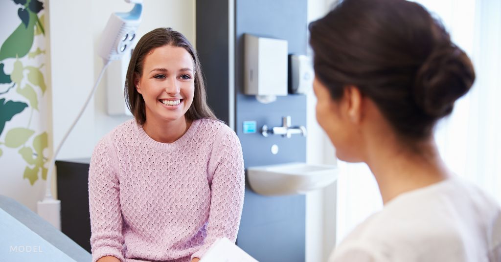 A woman smiling while talking to a female doctor. (Model)